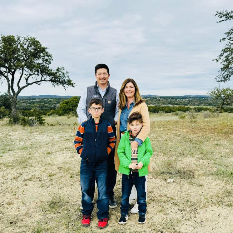 A husband and wife and their two sons standing in a field smiling at the camera.
