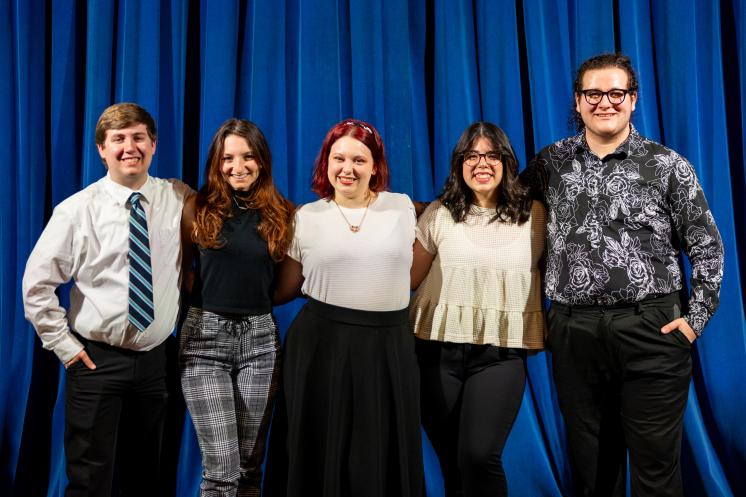 Alpha Psi Omega Group Photo A group of five smiling people standing together in front of a blue curtain.