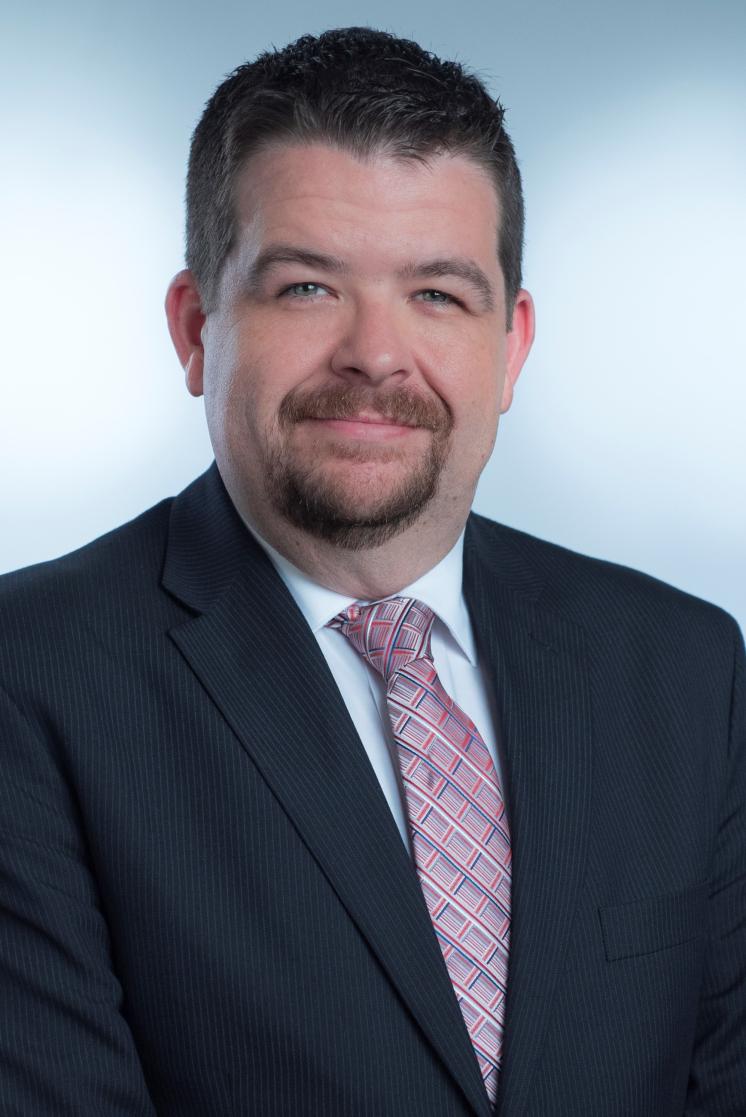 Man in dark suit with purple tie smirking at the camera.