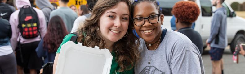 Two women smiling at the camera with food in their hands
